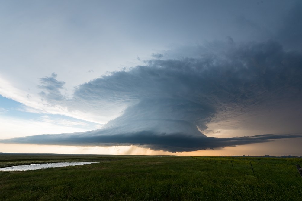 1. A large, dark storm cloud looms over a green field, indicating impending rain and severe weather conditions.