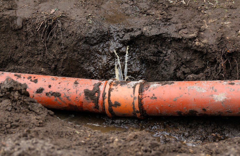 A broken pipe end rests in muddy ground, indicating potential damage or disrepair in the surrounding area.